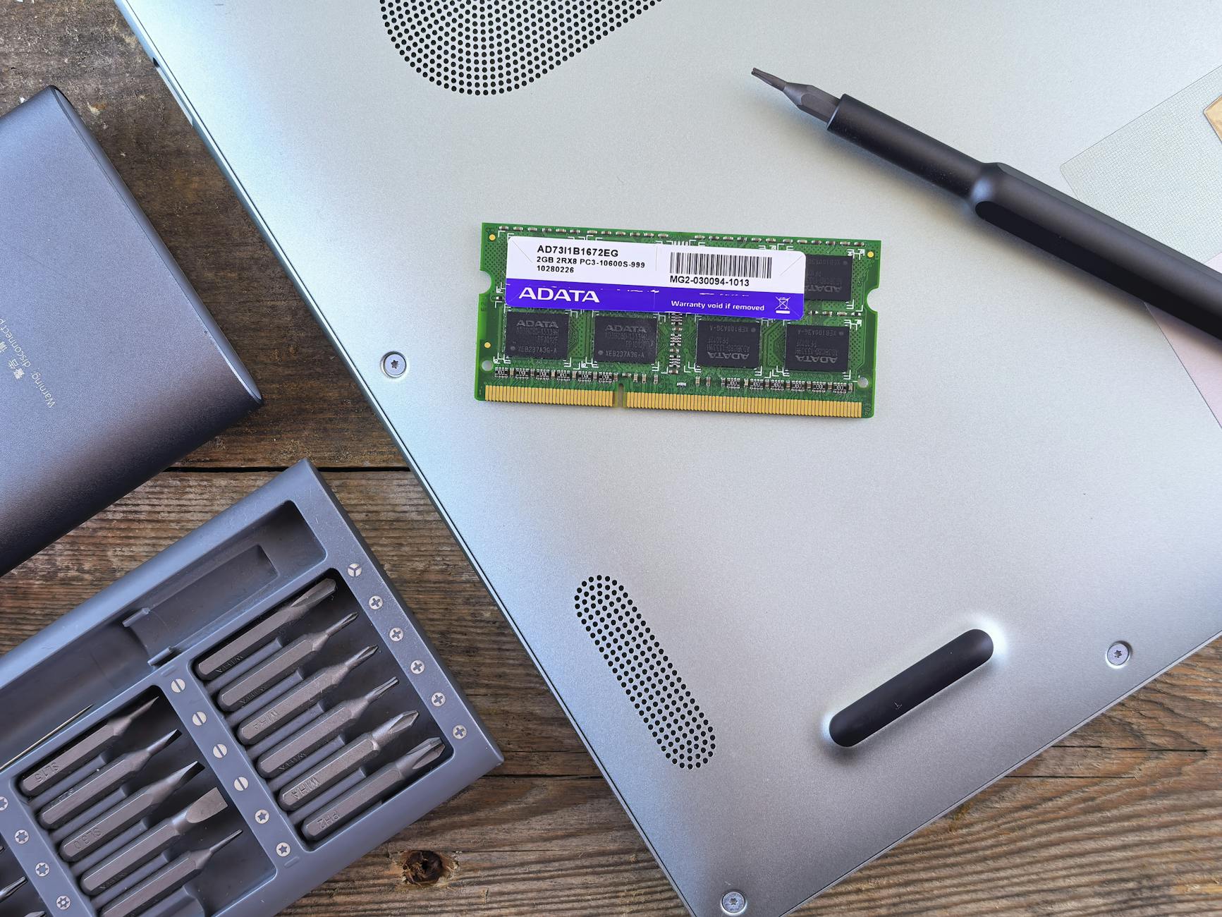 Close-up of an open laptop with RAM module, screwdriver, and toolset on a wooden surface.