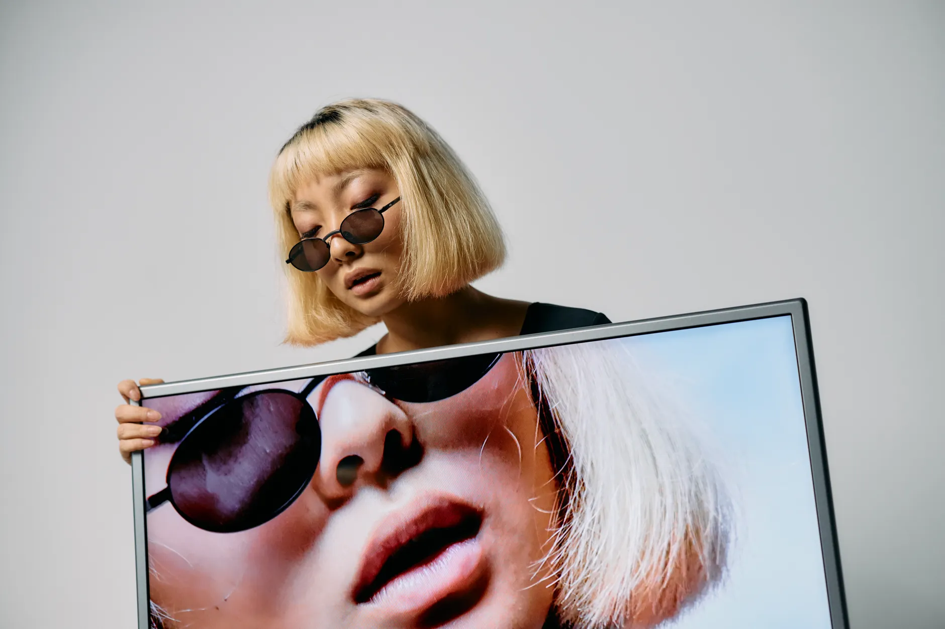 Studio photoshoot featuring a stylish model with sunglasses and a monitor display, blending fashion and technology.